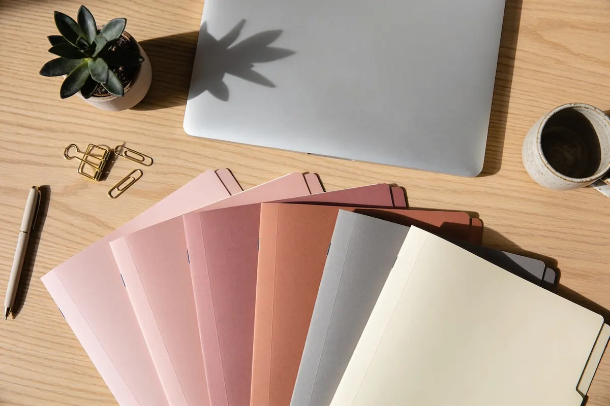 Ordner in Rosa, Grau und Creme, ordentlich auf einem Eichentisch aufgereiht